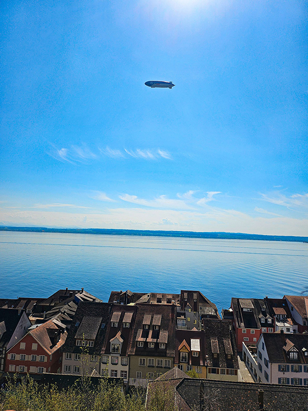 Zeppelin in an almost cloudless sky, rooftops of buildings at the bottom of the image.