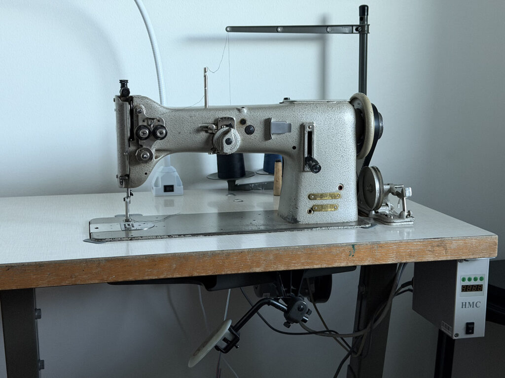 An old industrial sewing machine, a Pfaff 138 with a new servo motor mounted under the table that drives the machine through a belt.