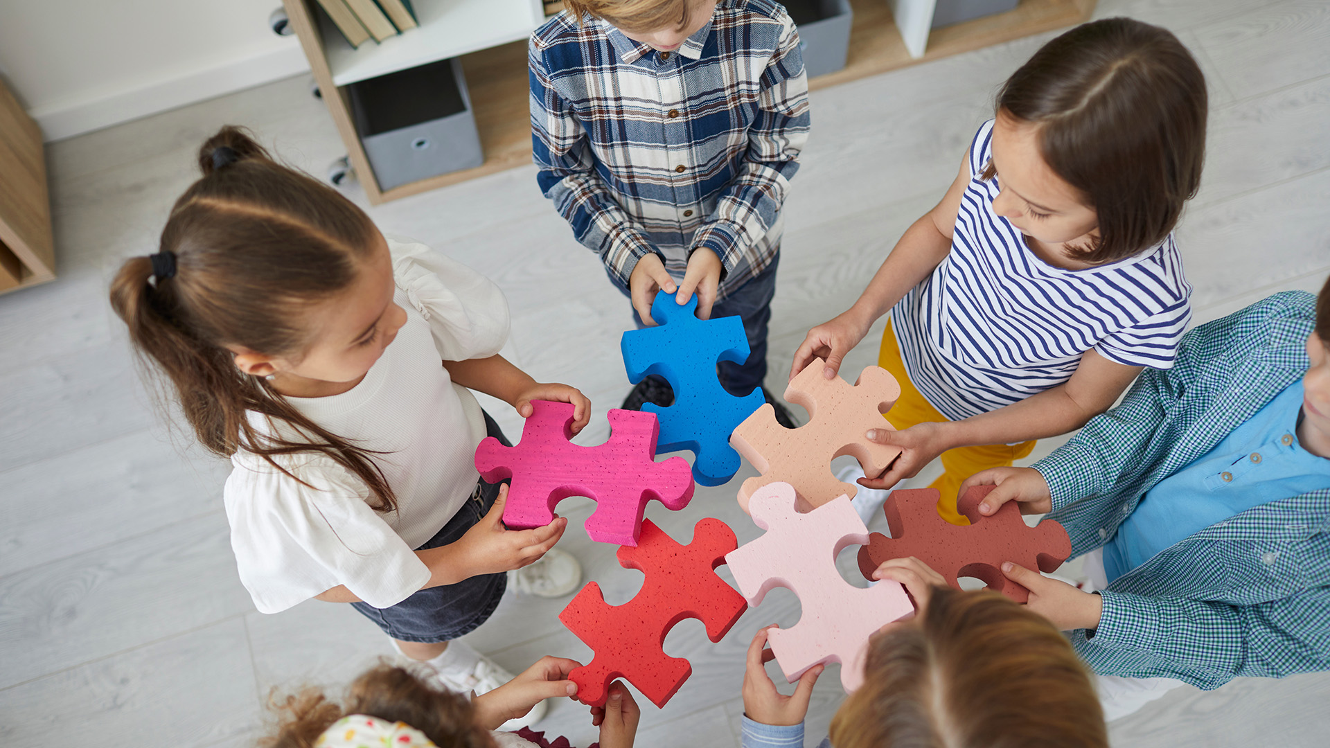Team of little children standing in circle and trying to join pieces of jigsaw puzzle